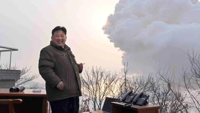 Kim Jong Un con un cigarro encendido y humo blanco proveniente del motor que se encuentra tras de él.